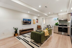 A modern living room with a sofa, a coffee table, and a TV. There is a kitchen area with a stove, oven, and cabinets. - Modern 2BR DC Stay near Union Market, NoMa & H Street (Washington)