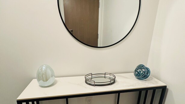 A white console table with a black metal frame, a round mirror above it, and a welcome sign on the left.