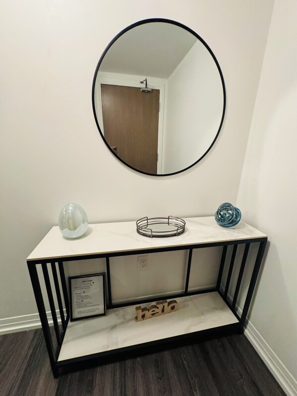 A white console table with a black metal frame, a round mirror above it, and a welcome sign on the left.