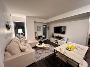 A modern living room with a sofa, coffee table, dining table, and a flat-screen TV. - 1 Bedroom condo in the heart of Downtown Toronto (Toronto)