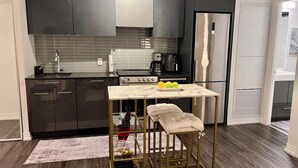 A modern kitchen with dark cabinets, a stainless steel refrigerator, a marble countertop, and a gold-framed stool.
