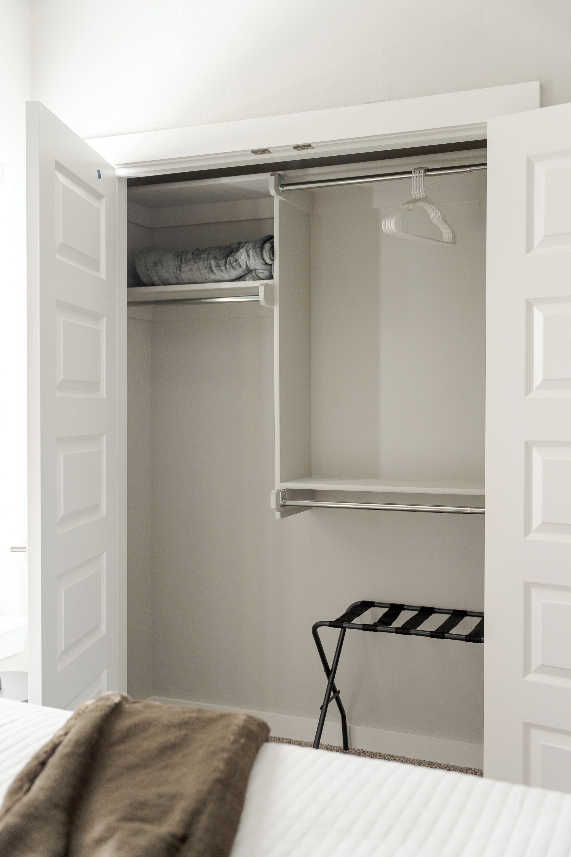 A white closet with open doors, a hanging rod, and a drying rack.