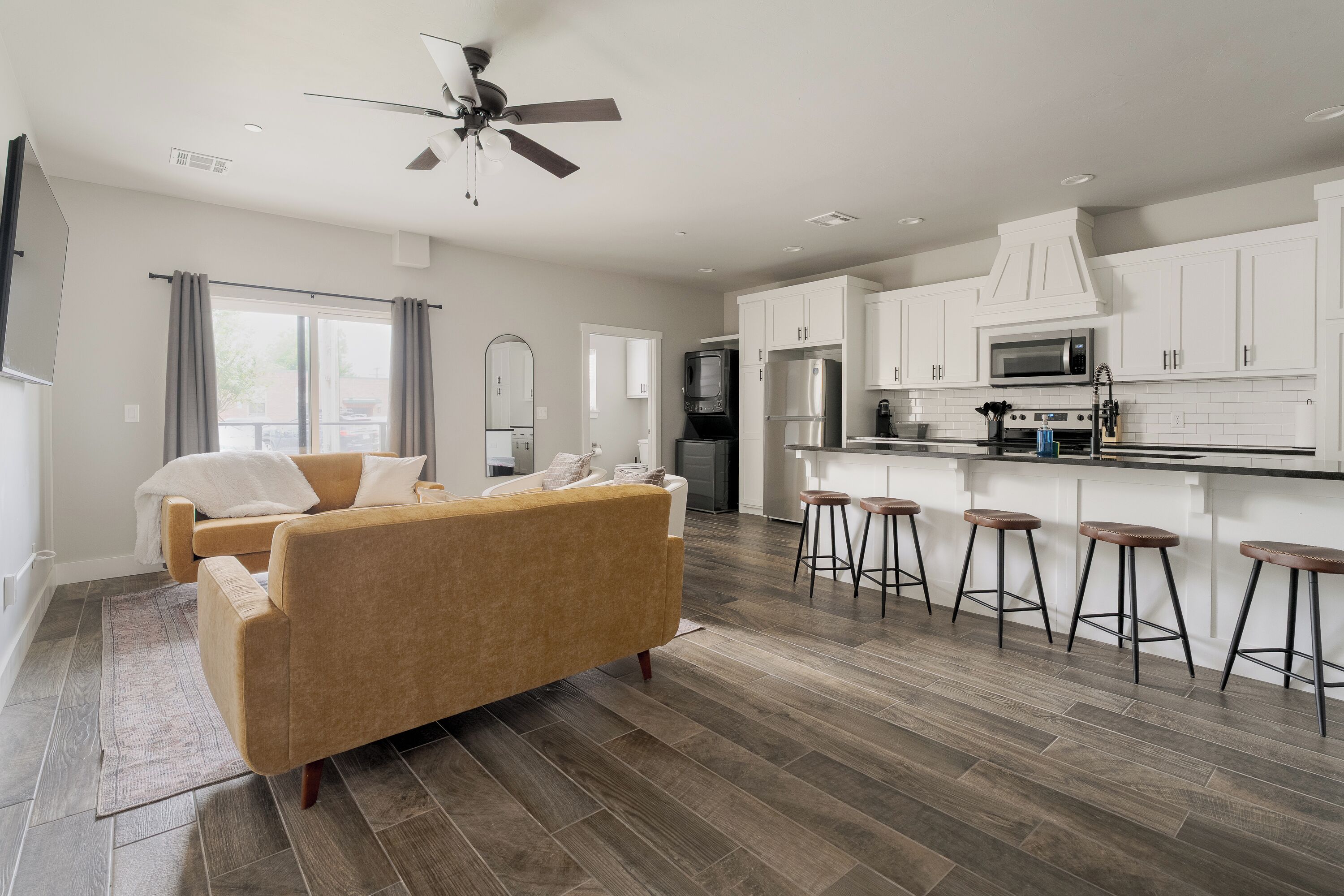A modern kitchen with white cabinets, a microwave, and a stove. There is a bar area with stools and a sofa in the living room.