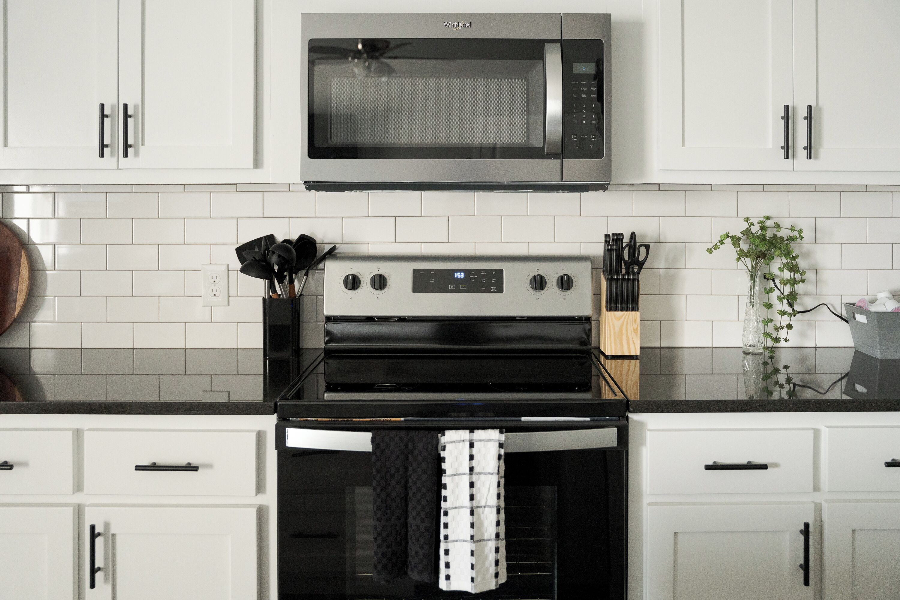 A kitchen with white cabinets, a stainless steel microwave, a built-in oven, and a black countertop.
