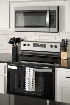 A kitchen with a stainless steel microwave, a stove, and a knife block. - E201: 3BR near UCO | 2 King+ Private Bath Every BR (Edmond)