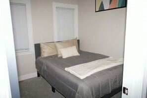 A bedroom with a bed, two windows, and a painting on the wall.