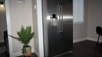 Un refrigerador de acero inoxidable en una habitación con una planta en maceta y una ventana.