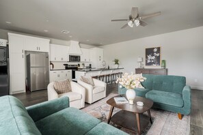 A modern living room with teal sofas, a white coffee table, and a kitchen in the background. - E301: 3BR near UCO | 2 King+ Private Bath Every BR (Edmond)