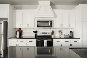 A modern kitchen with white cabinetry, a stainless steel refrigerator, a microwave, and a black stove. - E301: 3BR near UCO | 2 King+ Private Bath Every BR (Edmond)