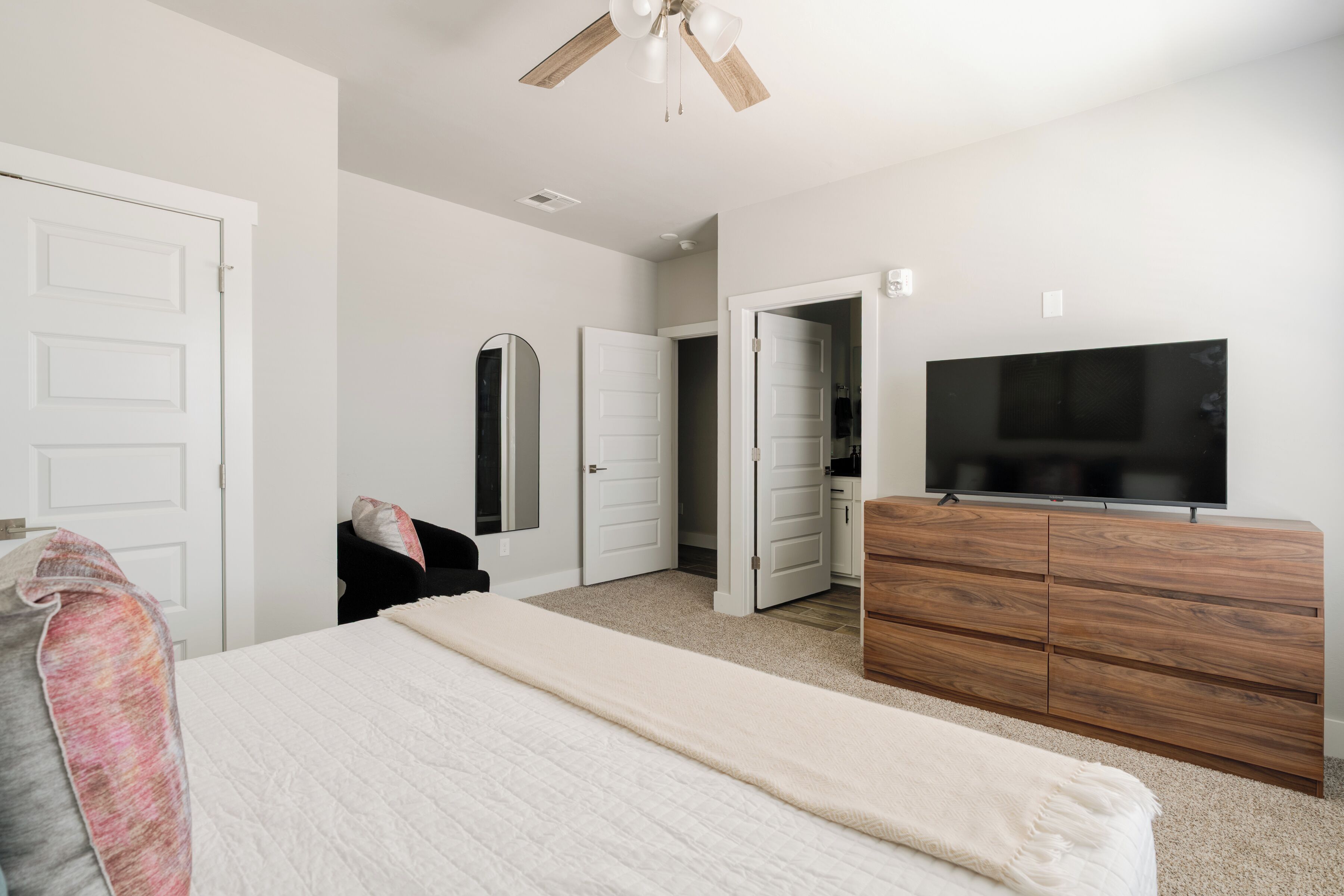 A bedroom with a bed, a dresser, a television, and a ceiling fan.