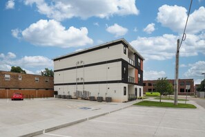 A multi-story building with a flat roof, large windows, and a parking lot in front. - E102: 3BR near UCO | 2 King+ Private Bath Every BR (Edmond)