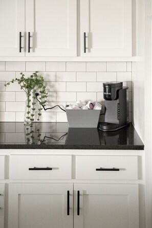 A kitchen with white cabinets, a black countertop, a Keurig coffee maker, and a vase with green plants. - E102: 3BR near UCO | 2 King+ Private Bath Every BR (Edmond)