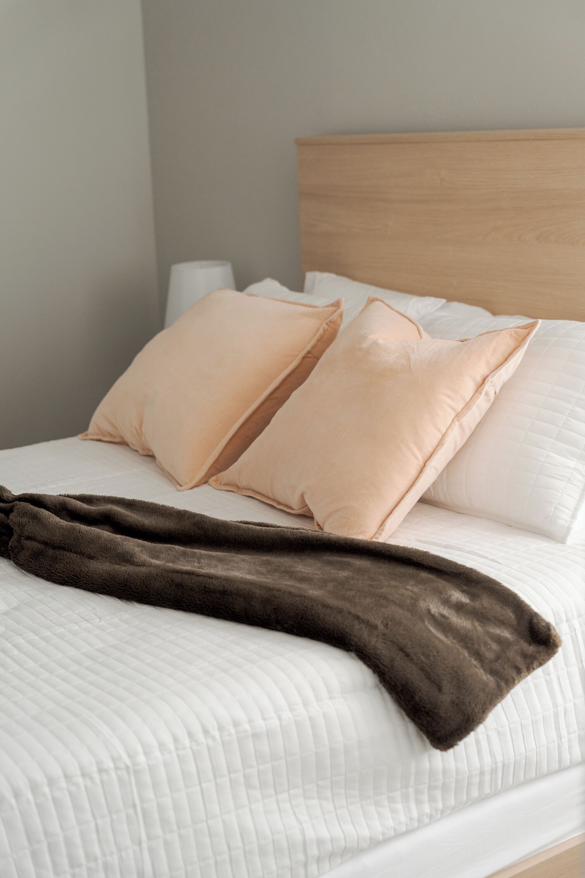 A bed with white bedding, two beige pillows, and a brown blanket.