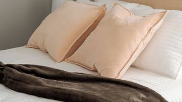A bed with white bedding, two beige pillows, and a brown blanket.