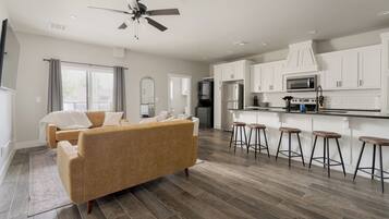A modern kitchen with white cabinets, a microwave, and a stove. There is a bar area with stools and a sofa in the living room.