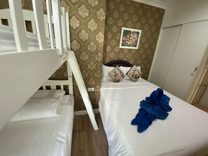 Ein Zimmer mit Etagenbetten, einem Bett mit Kissen und einer blauen Decke sowie einer Wand mit einem Blumenmuster.