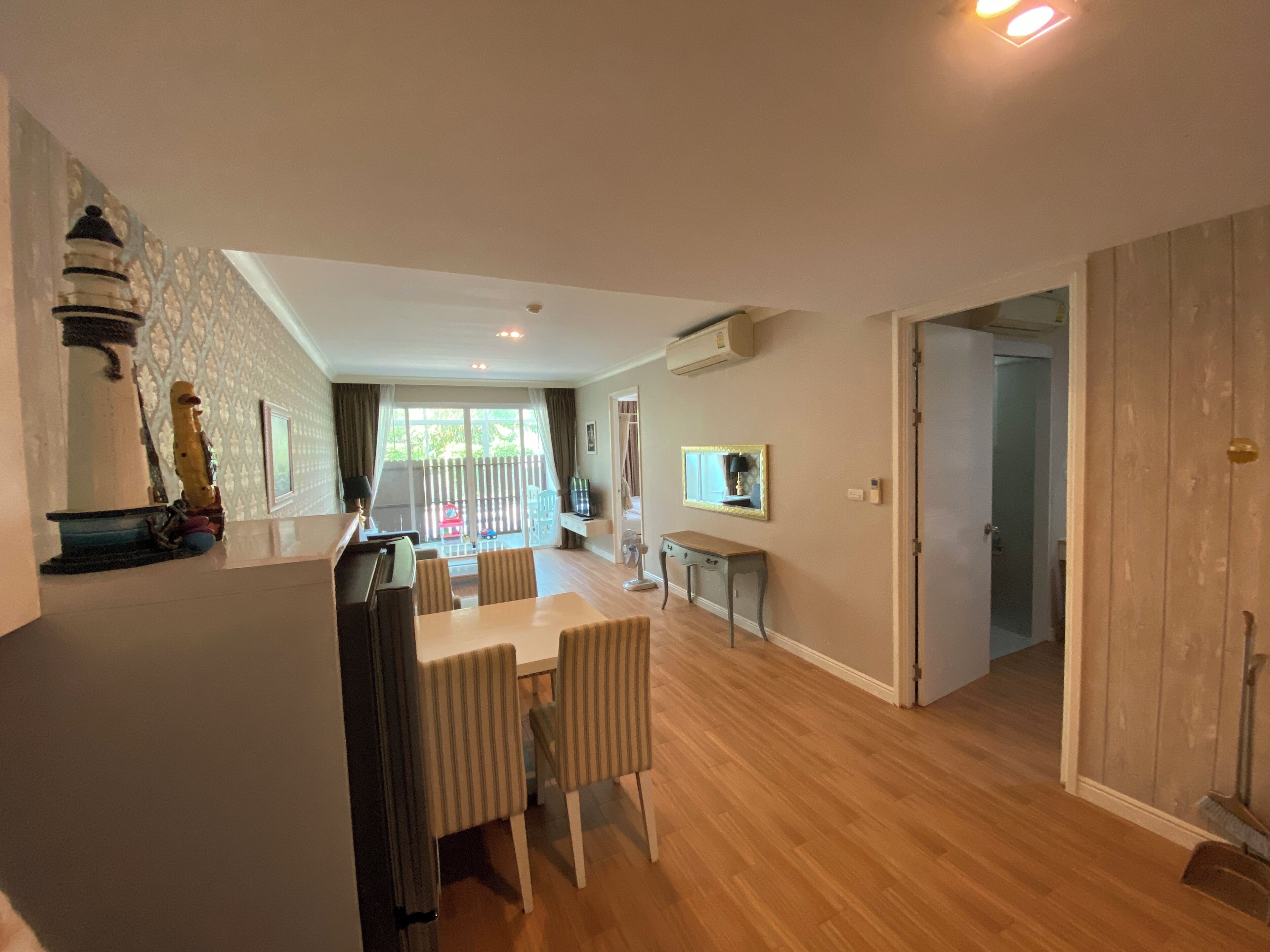 A spacious living area with a dining table, chairs, a television, and a sliding door leading to another room.