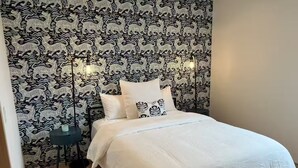 Una camera da letto con carta da parati decorata, un letto con biancheria bianca e un comodino con una lampada.