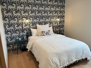 Une chambre à coucher avec un papier peint à motifs, un lit recouvert de draps blancs et une table de chevet avec une lampe.