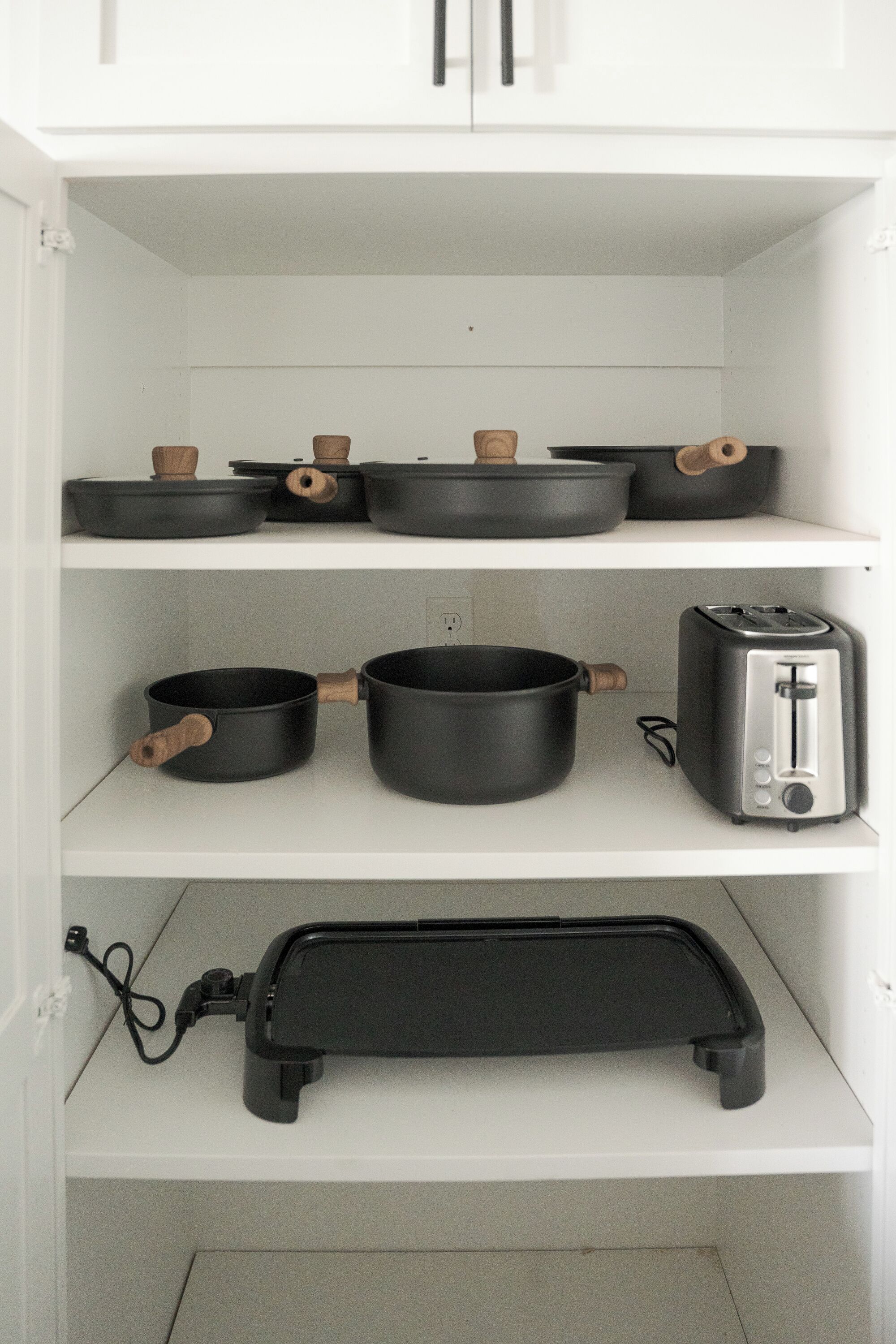 A kitchen with white cabinets, black pots with wooden handles, a toaster, and a black appliance with a cord.