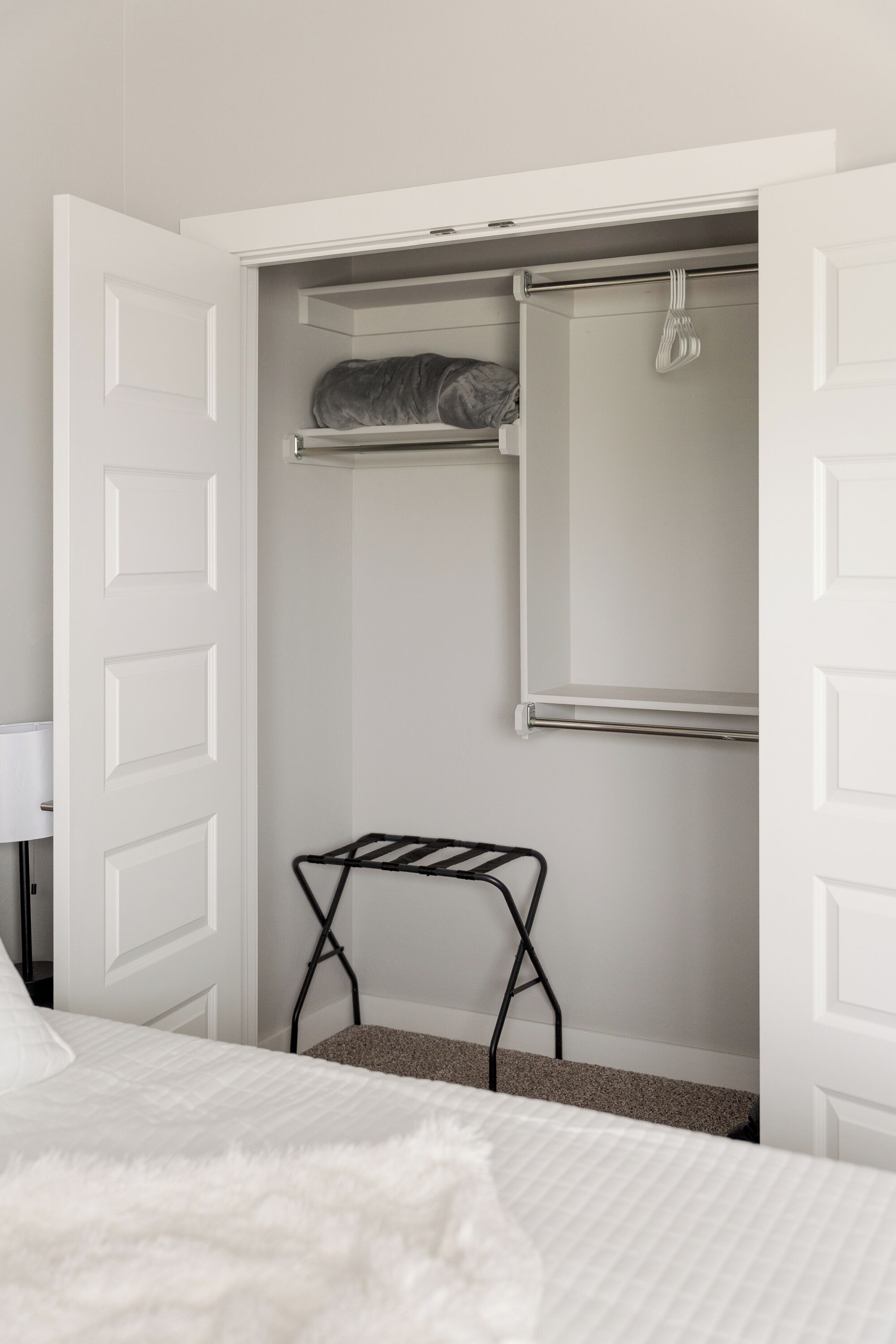 A bedroom with a bed, a white wardrobe, and a black drying rack.