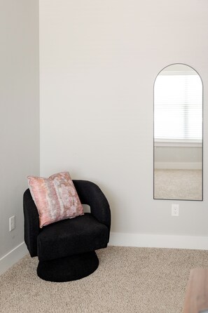 A room with a black armchair, a single wall-mounted mirror, and a carpeted floor. - E202: 3BR near UCO | 2 King+ Private Bath Every BR (Edmond)