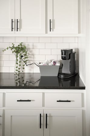 A kitchen with white cabinets, a black countertop, a Keurig coffee maker, and a vase with green plants.