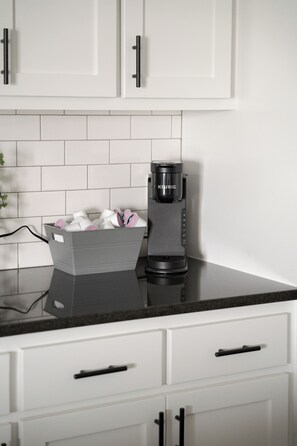 A modern kitchen with white cabinets, a black countertop, and a coffee maker.