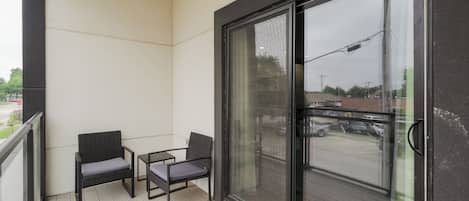 Un balcon avec deux chaises et une petite table, une porte-fenêtre coulissante et une vue sur la rue.