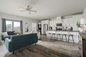 A modern kitchen with white cabinets, a central island with bar stools, and a ceiling fan.