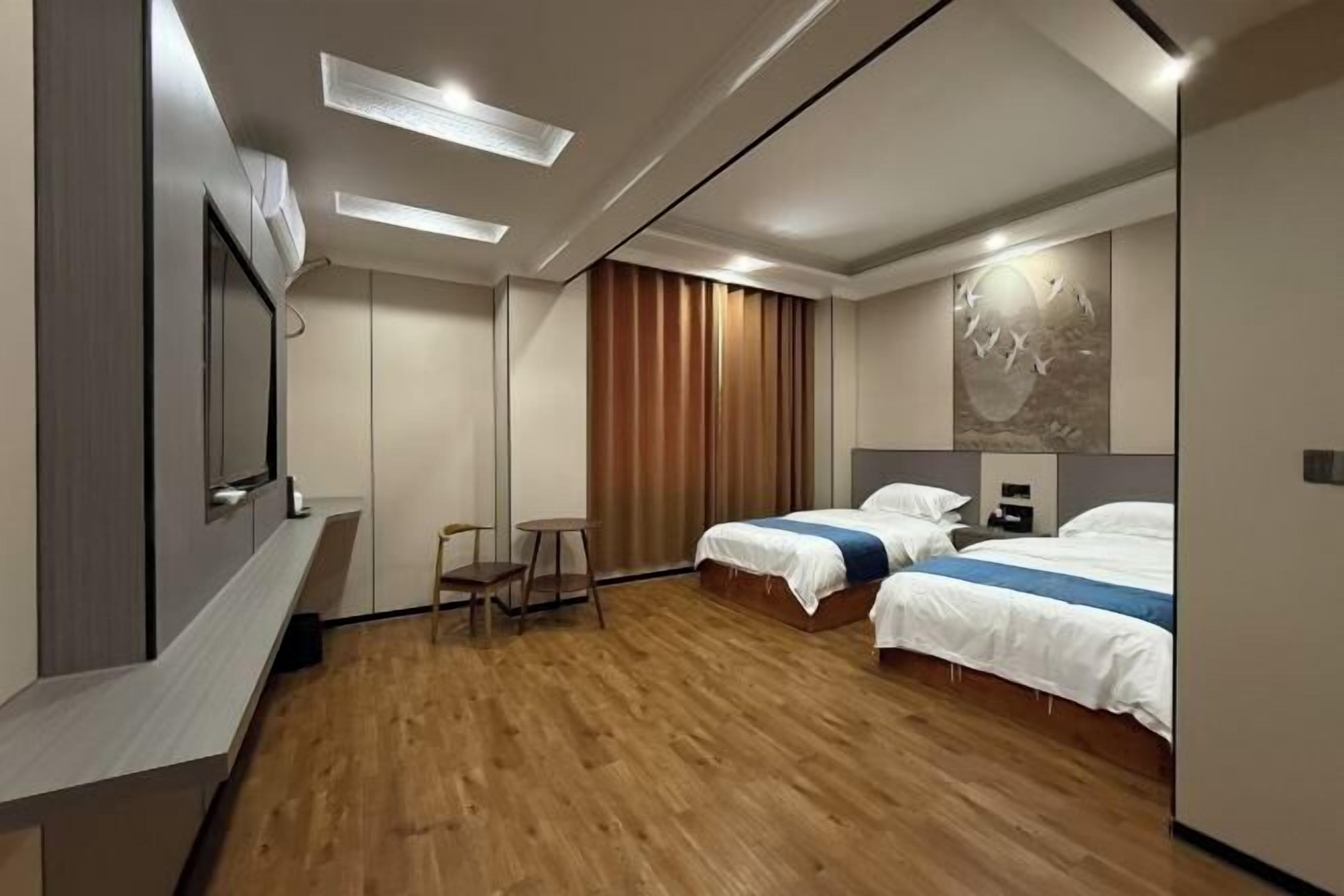 A hotel room with a wooden floor, a bed, a desk, and a chair.
