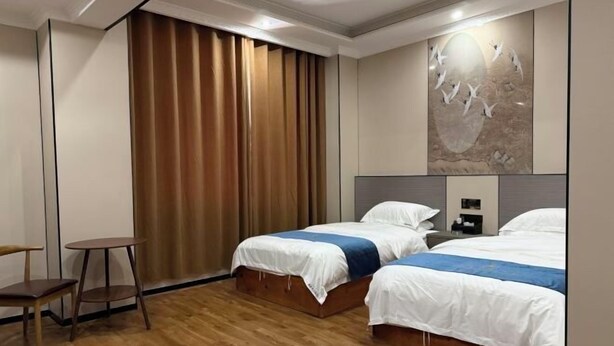 Une chambre d’hôtel avec deux lits, un plancher en bois, un bureau et une grande fenêtre avec des rideaux.
