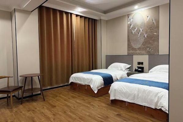 A hotel room with two beds, a wooden floor, a desk, and a large window with curtains.