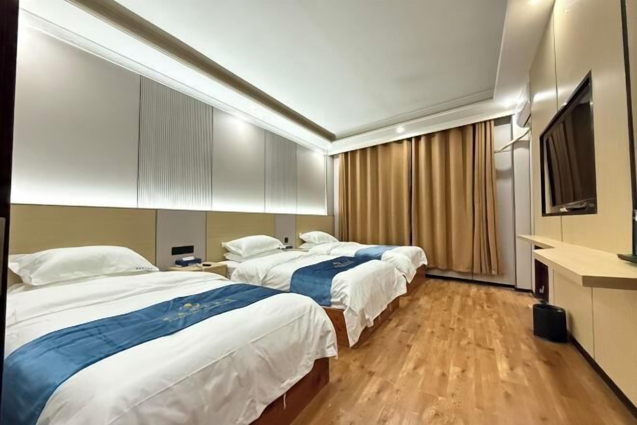 Ein Hotelzimmer mit drei Betten, Holzboden, einem großen Spiegel und einem Fernseher.