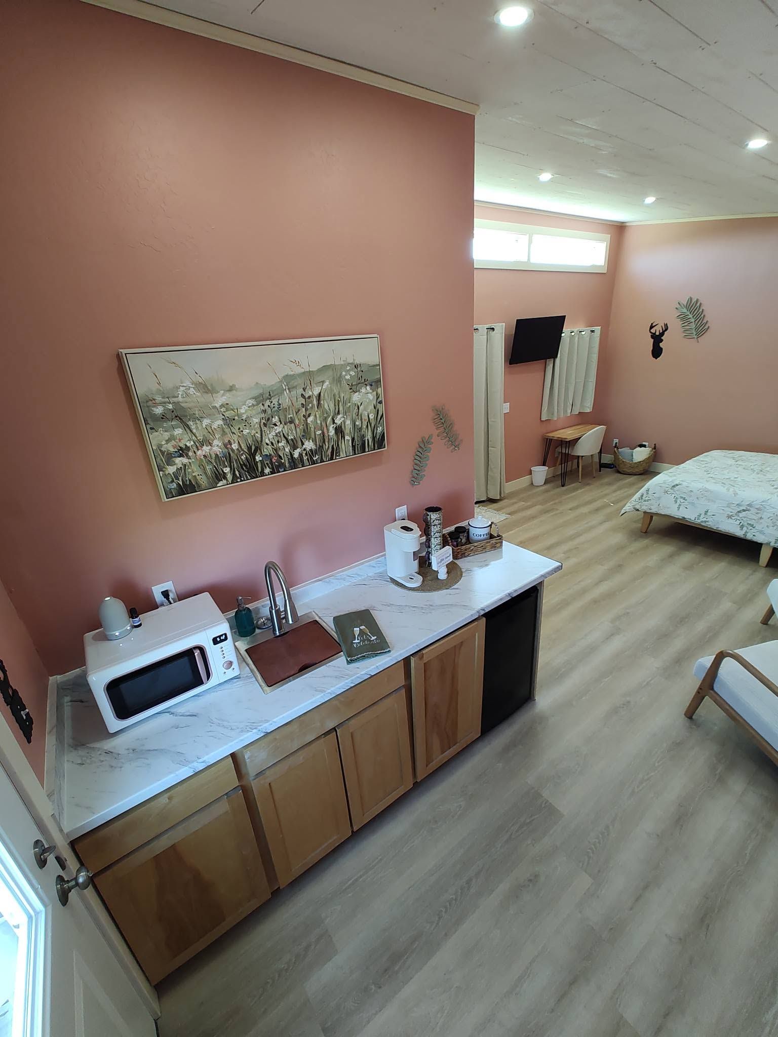 Een moderne keuken met een marmeren aanrechtblad, houten kastjes en een spoelbak. Boven de spoelbak hangt een schilderij en aan de muur is een decoratie van een hertenkop bevestigd.