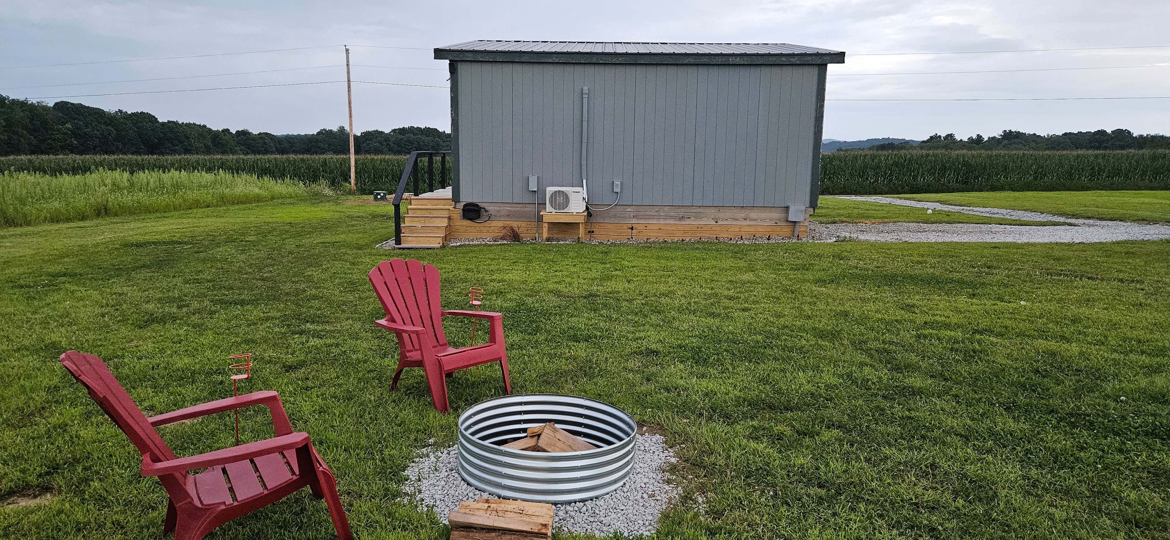 A grassy outdoor area with a metal shed, two red chairs, and a metal fire pit.