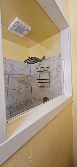 A shower enclosure with a white frame, marble tiles, and a handheld showerhead.