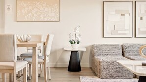 Ein modernes Wohnzimmer mit Essbereich, ausgestattet mit einer Couch, Sesseln, einem Tisch und einer Vase mit Blumen.