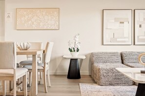 Ein modernes Wohnzimmer mit Essbereich, ausgestattet mit einer Couch, Sesseln, einem Tisch und einer Vase mit Blumen.