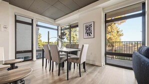 Ein modernes Interieur mit Essbereich, einer Couch und großen Fenstern mit Blick ins Freie.