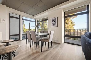 Ein modernes Interieur mit Essbereich, einer Couch und großen Fenstern mit Blick ins Freie.