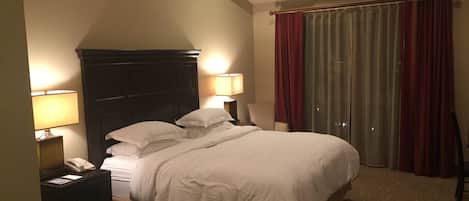 Una habitación de hotel con cama, lámparas de noche, teléfono, una silla y una ventana con cortinas.