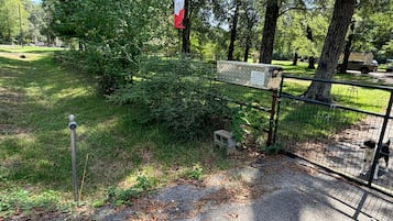 Un parque cercado con un perro, árboles y una bandera.