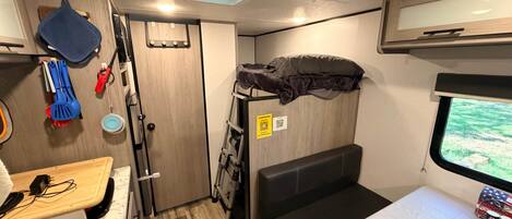 A compact interior with a bunk bed, a small kitchenette, and a window providing a view.