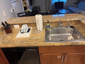 A kitchen with a granite countertop, stainless steel sink, and a dish soap bottle.