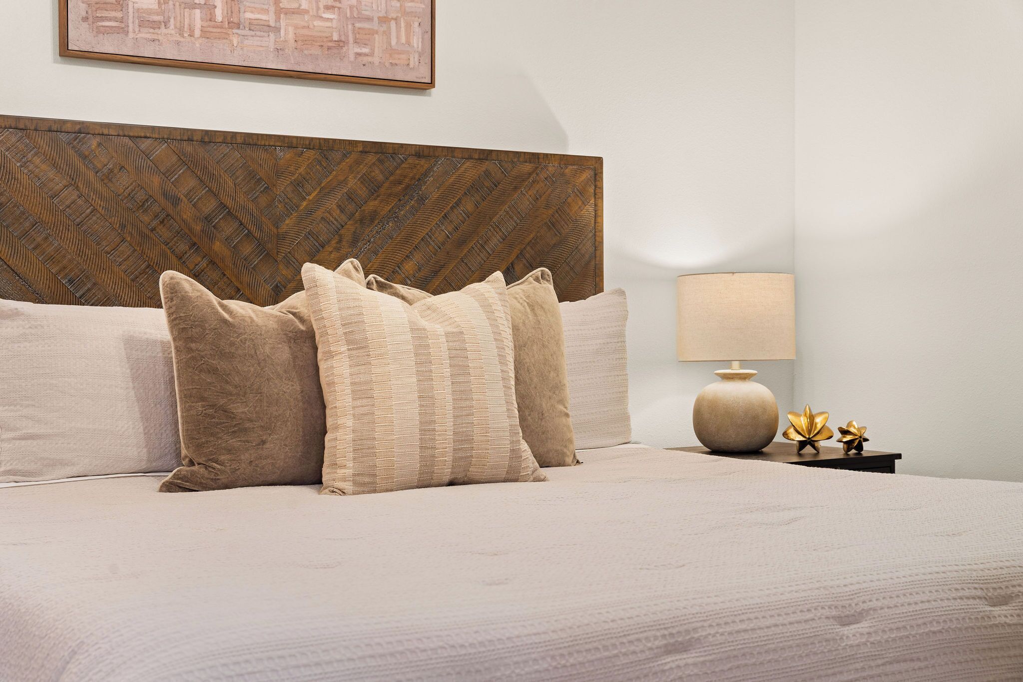 Un letto ben rifatto con diversi cuscini, una testiera in legno, un comodino con una lampada e un quadro appeso alla parete.