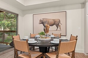 Een eetgedeelte met een ronde tafel voor zes personen, omringd door houten stoelen met beklede zitplaatsen. Een groot kunstwerk van een stier hangt aan de muur, en op tafel staat een decoratieve boomsculptuur.