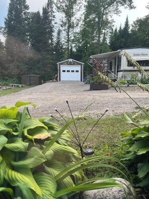 Ein Schotterweg führt zu einer weißen Garage, umgeben von üppiger Bepflanzung und einer Wohngegend.