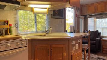 A compact RV kitchen with a stove, sink, and wooden cabinets.