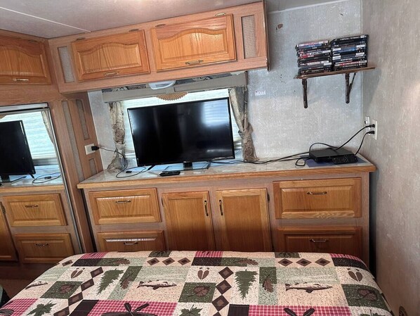 Un dormitorio con cama, armarios de madera, televisor y estantería con libros.